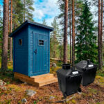 Stor-Jukka dasspaket med modern blå utedassbyggnad och två Green Toilet 330 komposttoalettbehållare i skogsmiljö