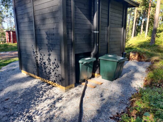 Green Toilet med extra behållare bakom utedass